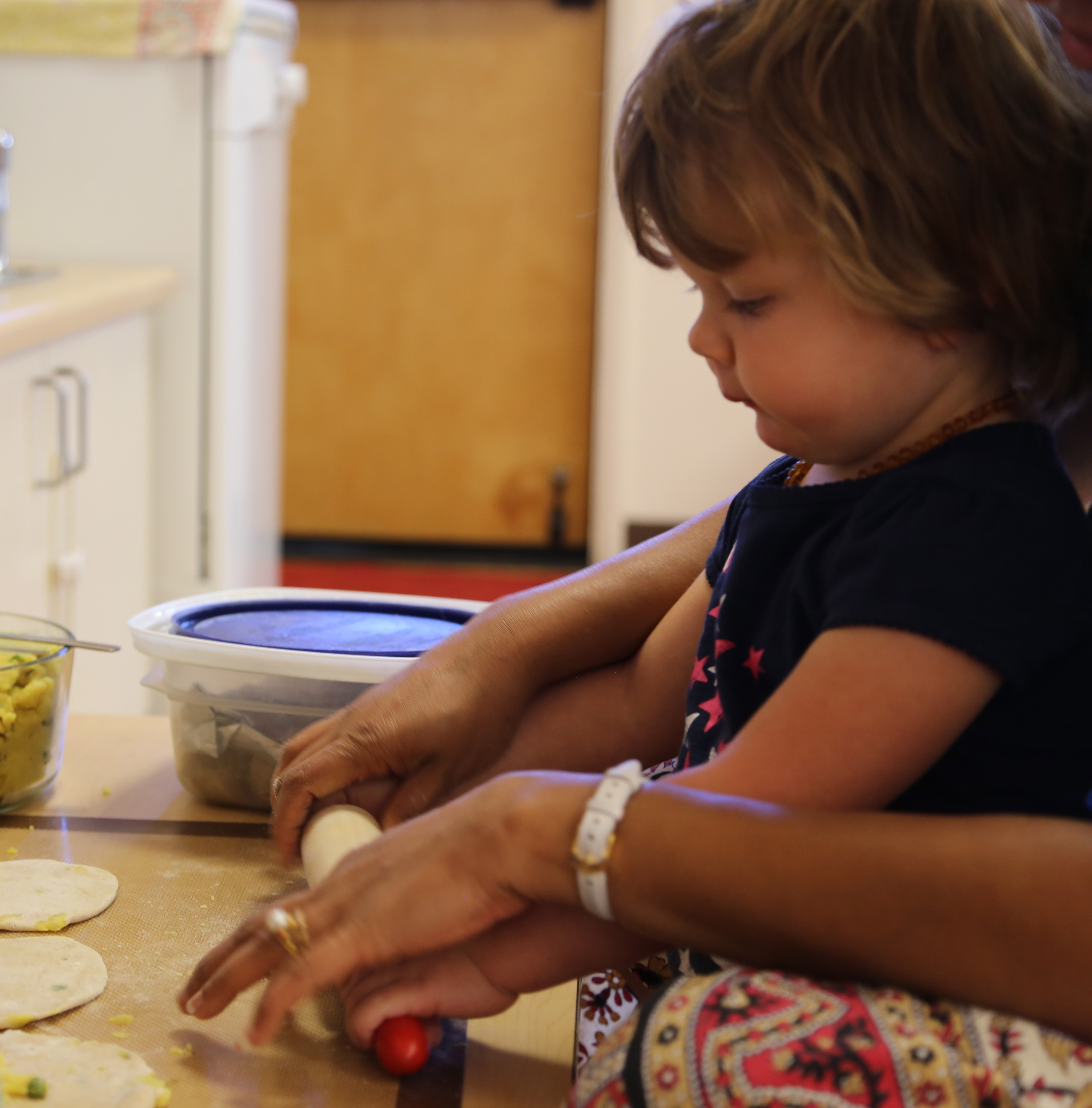 Toddler using a rolling pin while teacher guides her in a Montessori classroom