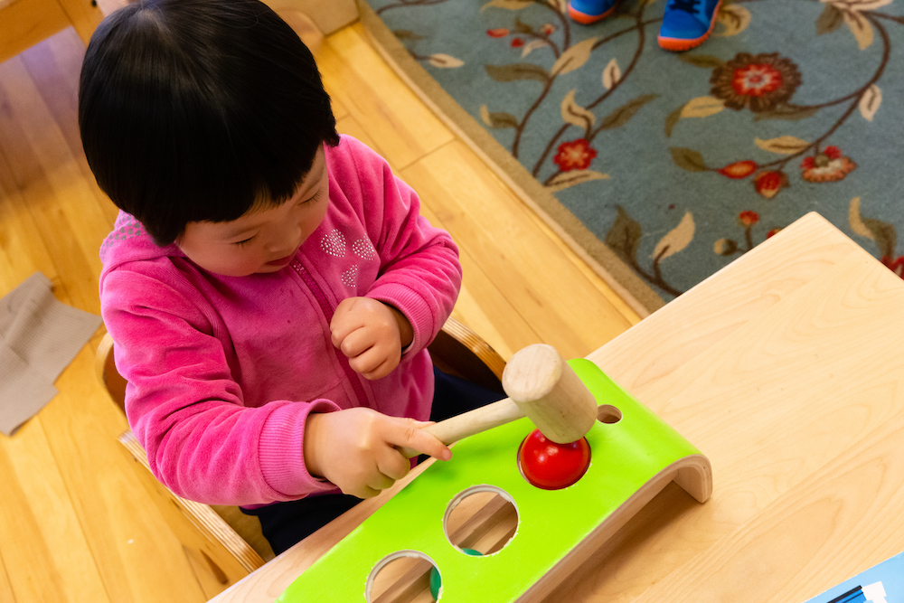 Girl in Montessori Classroom using a wooden hammer toy