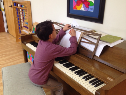 Boy writing music with a piano in a Montessori Elementary classroom