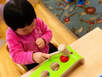 Girl in Montessori Classroom using a wooden hammer toy