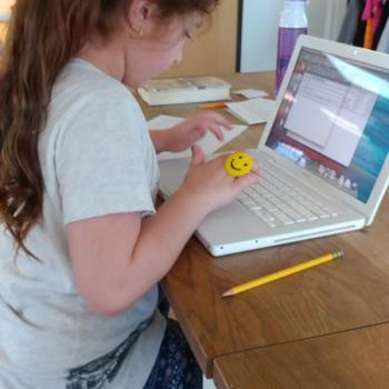 Girl sitting at desk Solving Problems Using a Laptop in Montessori classroom