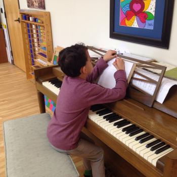 Elementary Montessori school child writing music and playing the piano
