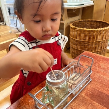 Toddler independently adding toothpicks into a small jar at Lifetime Montessori School 